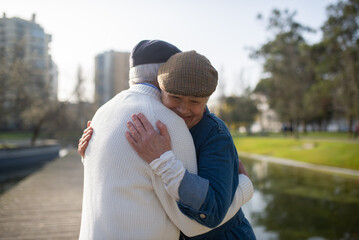 Portrait of senior couple during romantic date. Caucasian man and woman standing near pond in city park gently hugging each other and feeling happy. Relations, leisure activity of aged people concept