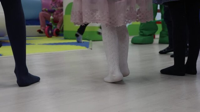 At the children's party in the entertainment room, host arranged a fun game competition for the children. A little girl in a princess dress stands modestly in a circle of friends at a birthday party