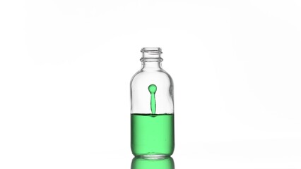 Drop of green liquid is falling down into clear medical bottle and make column splash inside it on white background | Abstract skincare cosmetics ingredients concept