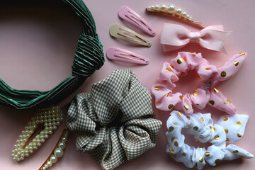 Colorful scrunchies, emerald green headband and pearl hair clips on pastel pink background. Flat lay.