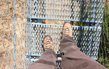 legs of the hiker with boots on while crossing a suspension bridge