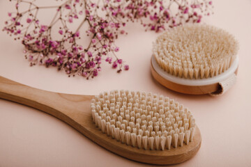 Dry wooden brushes for self home massage near a purple gypsophila on a pink background. Spa and body care concept