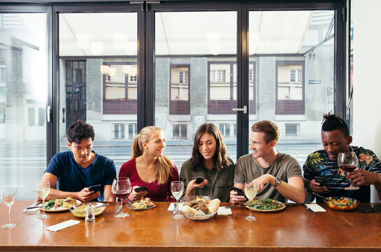 Friends having meal and looking at smart phones in restaurant