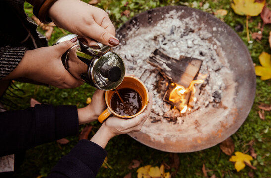 Overhead view of coffee being poured into mug above fire pit at picnic