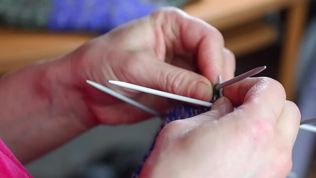 A housewife knits wool socks from blue threads on knitting needles.Close-up. Full HD slow motion video