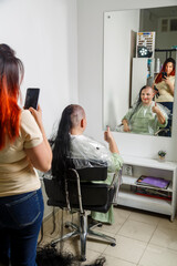 Woman smiling with half shaved head in barber chair hairdresser taking photo.