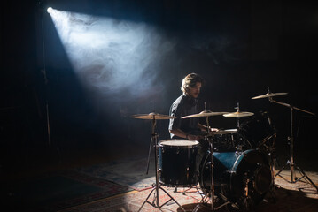 Young drummer sitting in spotlight and training in hall. Concentrated rock musician rehearsing or...
