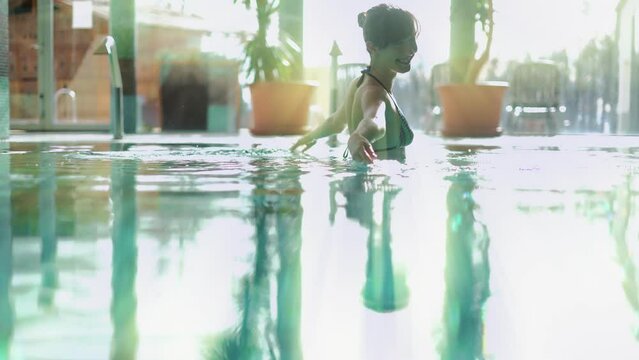 Wellness - white woman in her 30s enjoying water in pool, smiling.