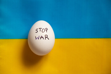Stop war is written on a white chicken egg that lies on the yellow-blue flag of Ukraine, a protest...