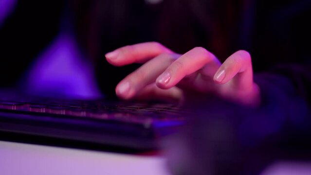 Close-up hand and keyboard playing games. Young woman sitting on chair with computer pc. Happy female Professional Streamer playing game online in dark room neon light.