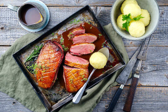 Traditional barbecue gourmet duck breast filet with skin served with potato dumplings in dark beer sauce as top view on a rustic metal tray