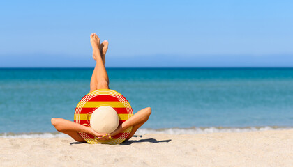 A slender tanned girl on the beach in a straw hat in the colors of the flag of Catalonia. Focus on the hat.