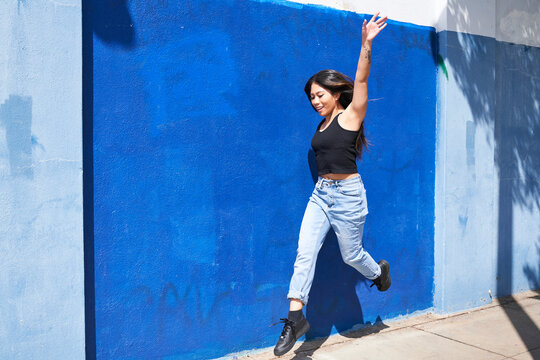Woman dancing and leaping in front of blue wall outdoors