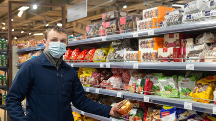 A man in a protective face mask chooses cookies. Sweet food. Quarantine