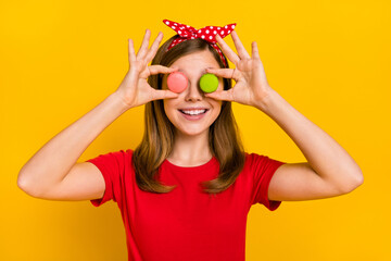 Portrait of cheerful positive little teenager childhood girl covering eyes with dessert isolated on yellow color background