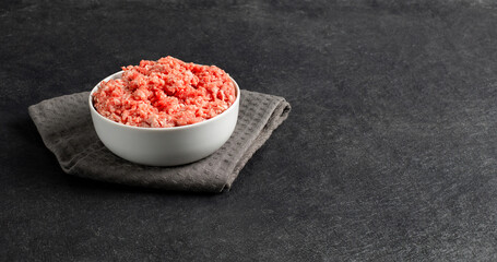 Fototapeta na wymiar Plate with fresh ground beef, textile on a gray black background, space for text, stock photo
