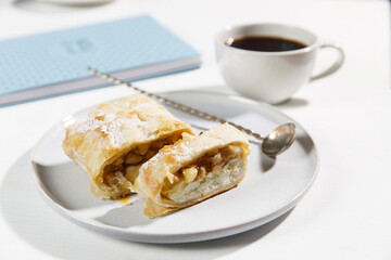 Apple charlotte with cottage cheese cream on a porcelain plate and a cup of tea on the table.