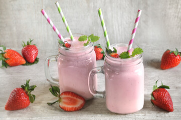Strawberry smoothie in mugs and scattered berries on a gray wooden background. selective focus