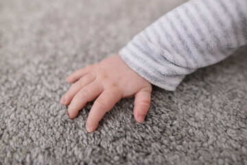 Baby hand touching grey new fluffy carpet surface. Closeup. Checking softness. Side view. Gentle and fluffy carpet between fingers.