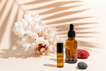 Brown glass cosmetic bottles with pipette, sea coral, sun shade tropical leaf on beige background. Natural cosmetics for face and body, aroma oil. Beauty summer concept. Products for branding, mock up