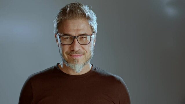 Portrait of happy older white man, glasses beard gray hair, smiling. Copy space for text gray background,