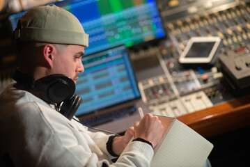 Concentrated young music producer taking notes in notepad. Man with headphones working in sound...