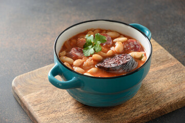 Asturiana traditional stew fabada with haricot, tomatoes, blood sausage on brown background. Close up.