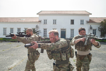 Portrait of courageous soldiers during battle. Men with blood smears on faces near house, aiming....