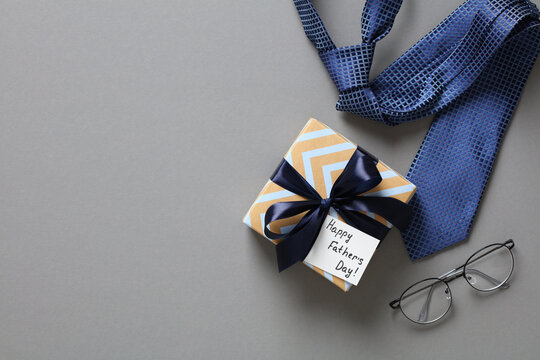 Happy Fathers Day concept. Flat lay composition with gift box, necktie, eyeglasses on grey background.