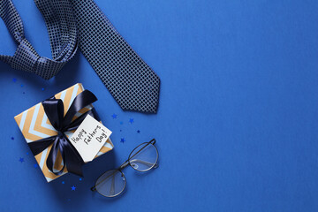 Happy Fathers Day flat lay composition with gift box, necktie, eyeglasses on blue table. Top view.