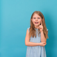 Fototapeta premium Portrait of a excited child pointing over blue background. Little girl points finger up. Copy space.