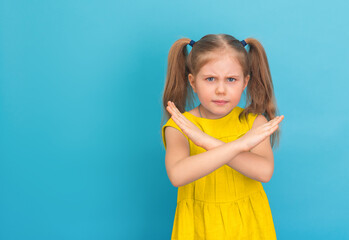 Little girl in yellow dress with negative expression on fer face showing stop gesture on blue...