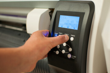 The printer operator presses the power button on the machine and starts printing. Man's hand and panel with buttons.