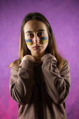 Pretty frightened woman with Ukraine flag on face isolated on dard background
