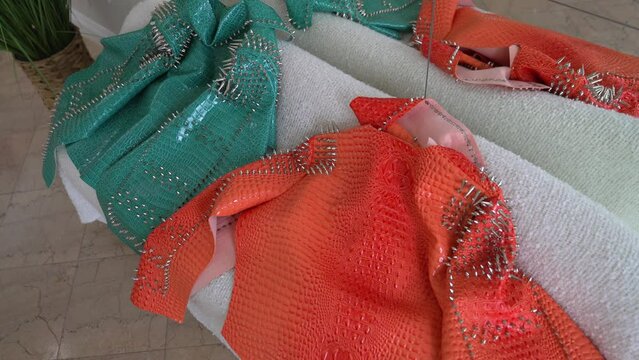 This panning video shows two bright colored alligator skin spiky studded jackets laying on a white modern couch.