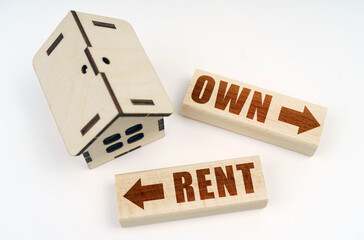 On a white surface, a wooden toy house and blocks with the inscription - Own or Rent