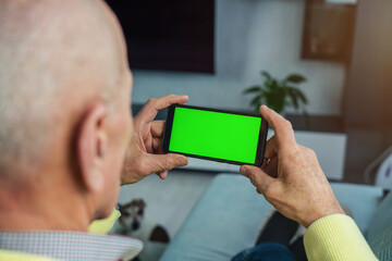 Mature person seated on sofa at home looking at blank green telephone screen closeup