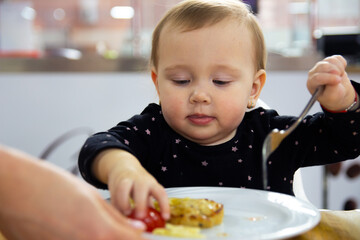 A little beautiful girl in a black dress eats food from a plate