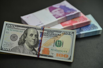 A heap of US 100 Dollar bills over Pak Rupee cash stacks of different denominations. Currency war concept, Falling Rupee value in Pakistan against US Dollar. Shallow depth of field. Selective focus.