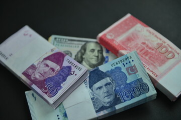 Stacks of Pak Rupee bills in different denominations over US 100 Dollar bills heap. Currency war concept, Falling Rupee value in Pakistan against US Dollar. Shallow depth of field. Selective focus.