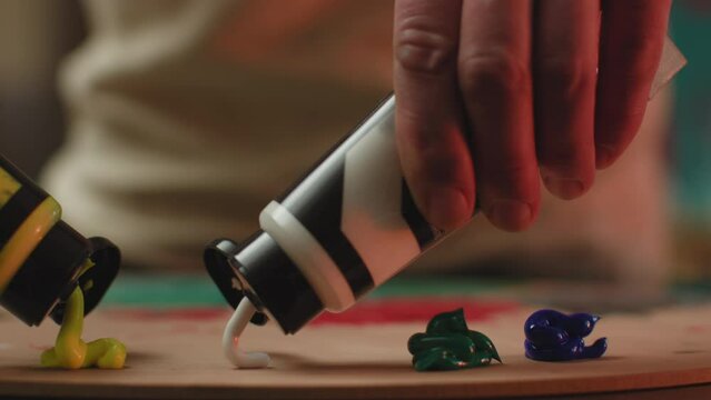 Artist routine. Painter hands squeeze acrylic paints from tubes on wooden palette. Closeup, prores codec. Creative hobby