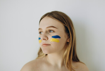 photo of a girl against a white wall with a ukrina flag on her cheeks