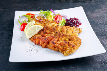 Traditional deep-fried schnitzel with green salad, tomatoes and cranberry jam served as close-up on a design plate