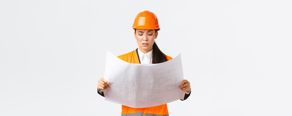Confused and doubtful asian female chief engineer, lead architect at construction area looking...