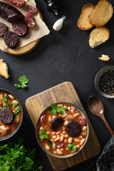 Two portions Asturiana spanish fabada with chorizo, morcilla, sausage, haricot served fresh toast on black background. Top view. Vertical format. Copy space.