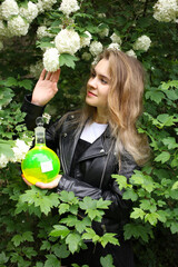 Portrait of a beautiful young female biochemist in the blooming bush holding a flask with green...