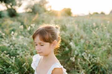 Fototapeta na wymiar Adorable little girl wearing natural white dress with wildflower motiv in green field with wild carrot flowers at summer, outdoor lifestyle. Freedom concept