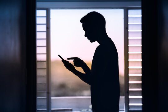 Male silhouette using smartphone indoors - Powered by Adobe