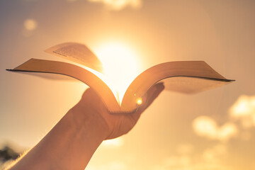 Hand holding open book bible up to the sunlight - Powered by Adobe
