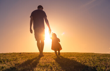 Silhouette of loving father walking side by side with child daughter holding hands.	